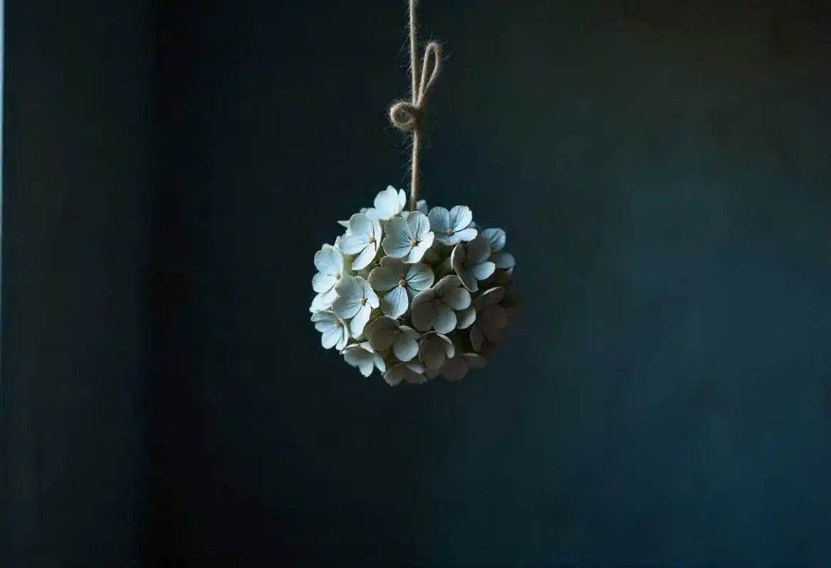 A creative hanging decoration made from small, light-colored dried Hydrangea florets tied with rustic twine, showcasing another method of How to Dry Hydrangea Flowers.