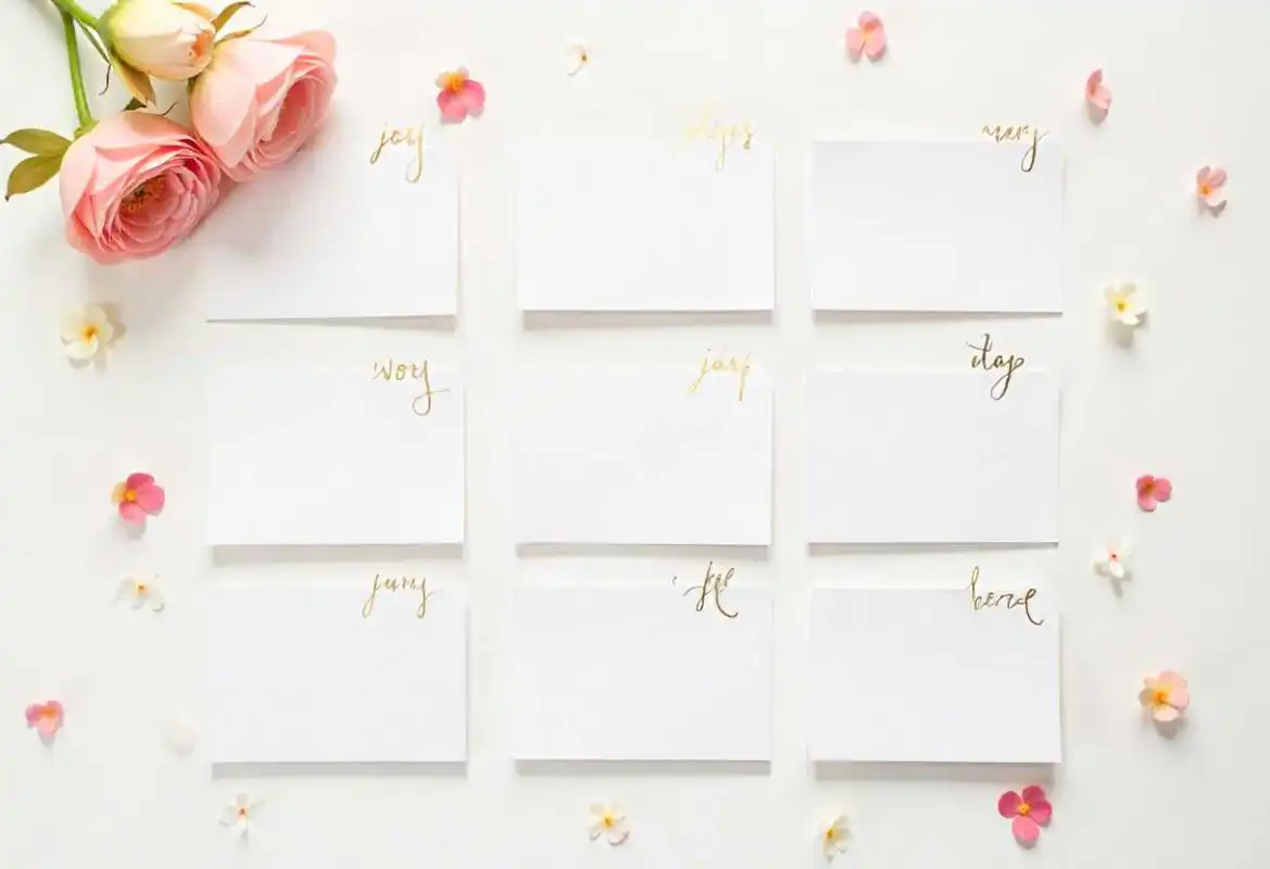 Birth Flowers for Every Month – Complete Guide for London 5 A flat-lay photo showing nine blank white cards with gold calligraphy, used to write the meanings of Birth Flowers for Every Month, beside pink roses.