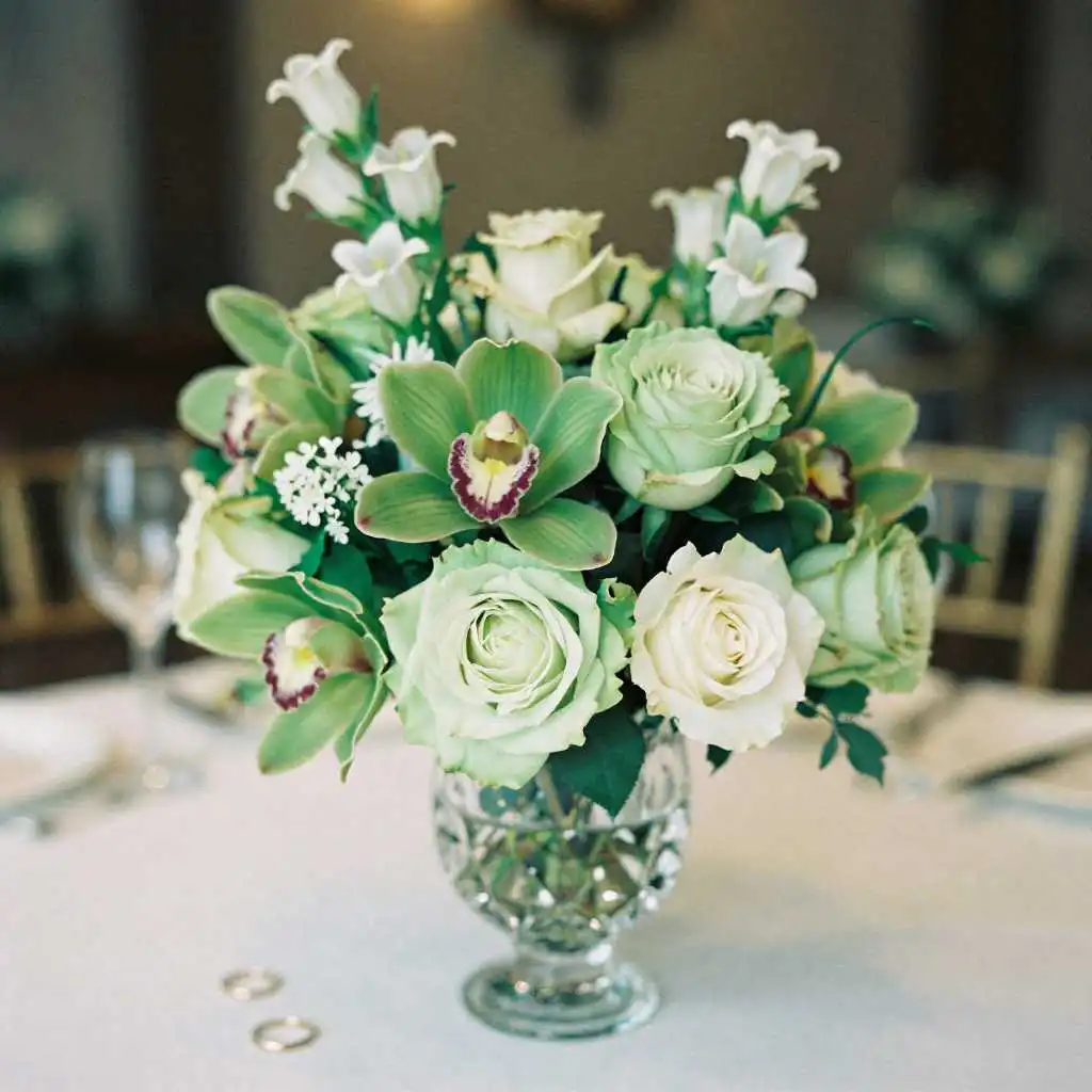 Green roses and orchids in crystal vase for 55th wedding anniversary celebration with couple celebrating in background