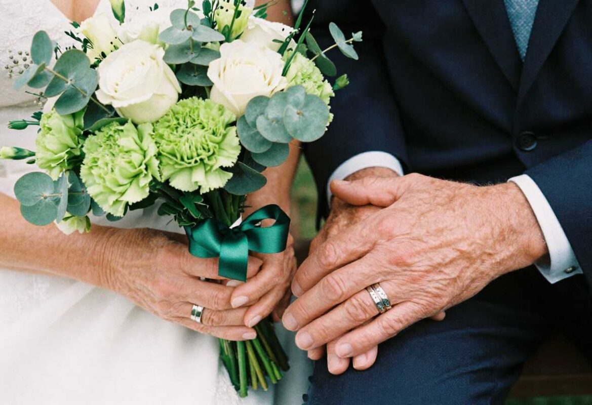 What Flower Is for 55th Wedding Anniversary? Complete Guide 3 Elderly couple holding mixed green flower bouquet with emerald ribbon for 55th wedding anniversary celebration